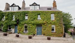 Old stone building covered in green ivy with blue doors and several windows, located on a cobblestone street