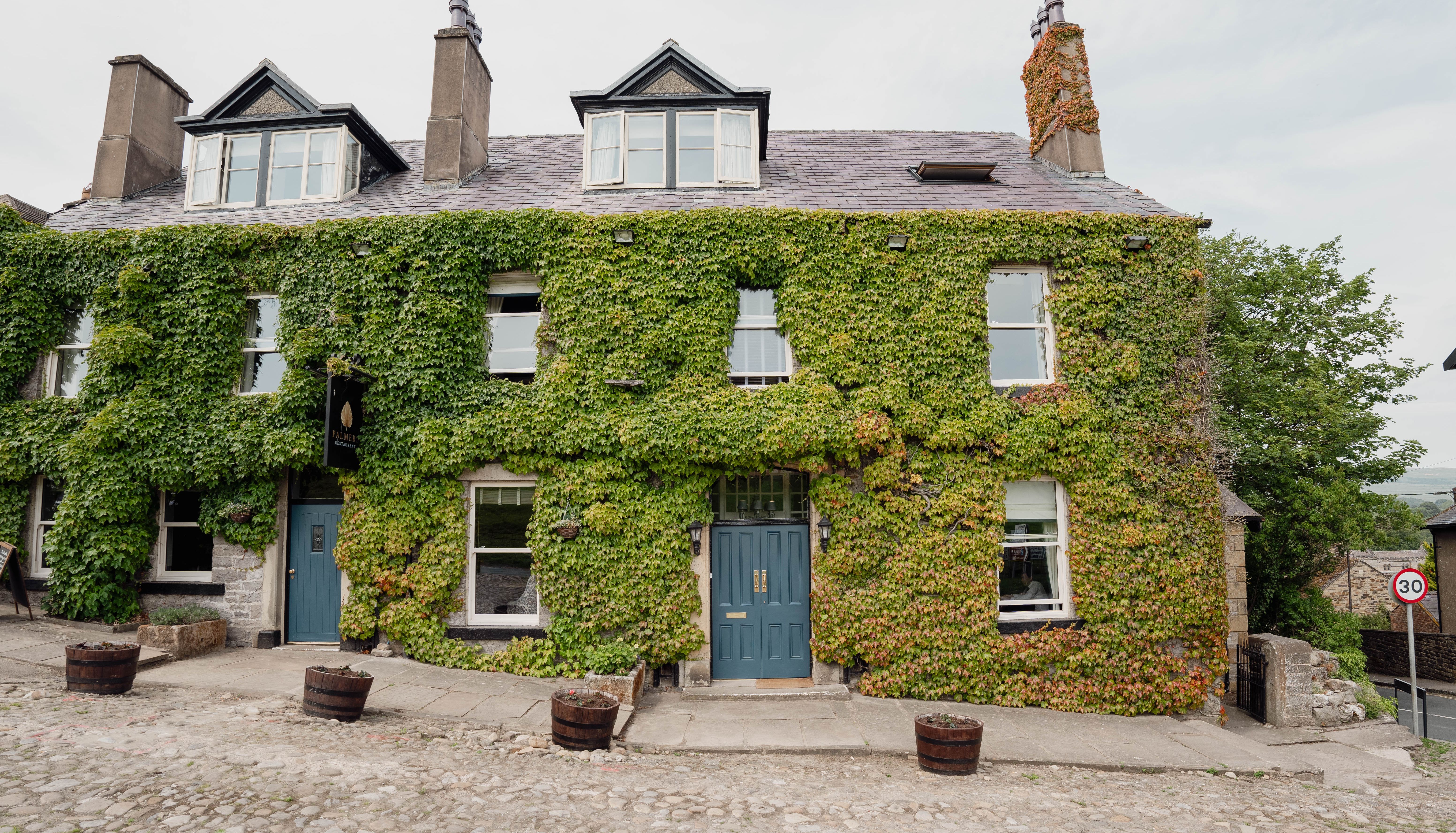 Old stone building covered in green ivy with blue doors and several windows, located on a cobblestone street