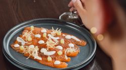 A plate of gourmet salmon sashimi with garnishes, next to a person holding a glass of white wine