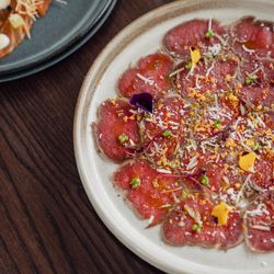 Plate of beef carpaccio garnished with edible flowers and greens on a wooden table