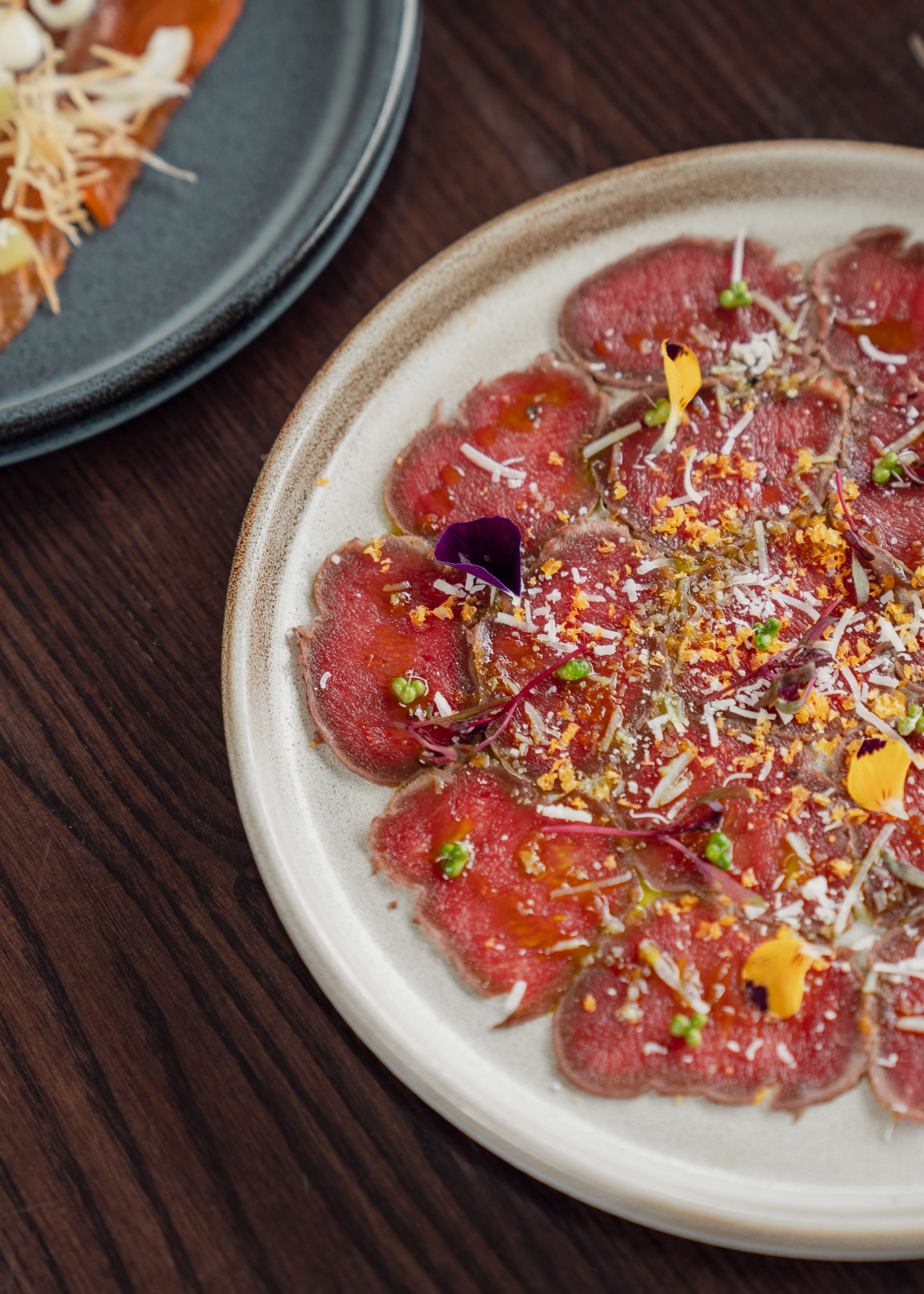 Plate of beef carpaccio garnished with edible flowers and greens on a wooden table