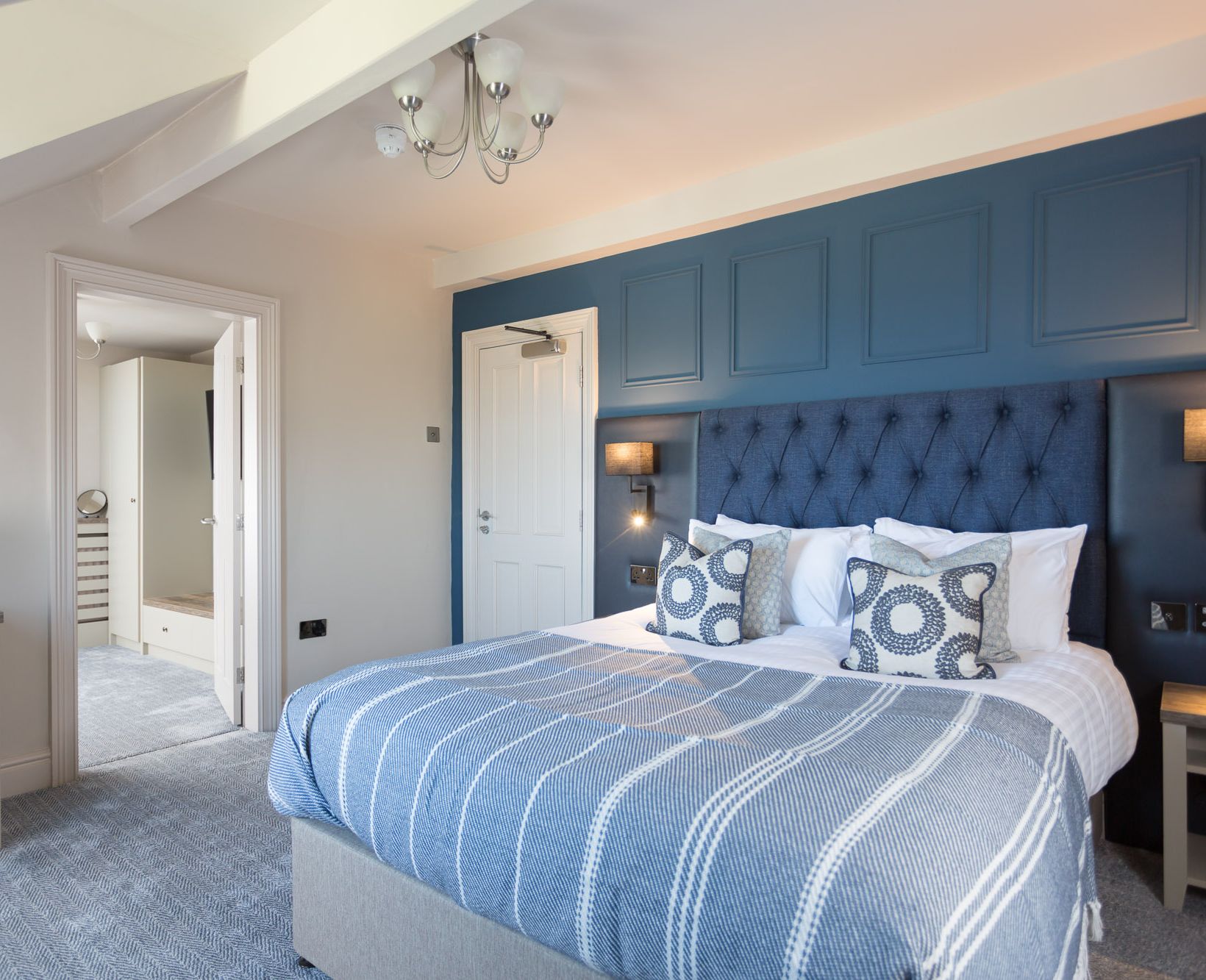 Modern hotel room with blue accent wall, large bed, and stylish decor