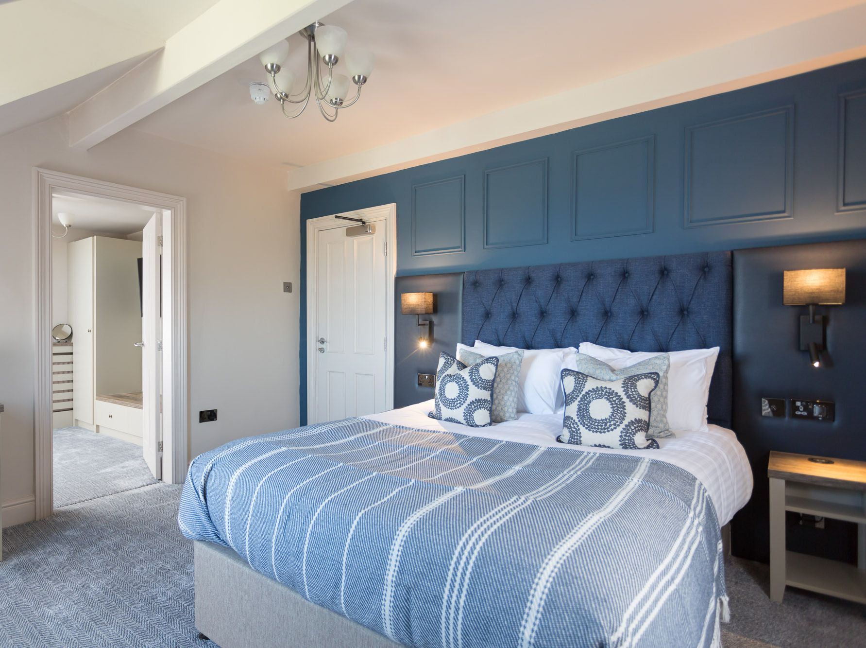 Modern hotel room with blue accent wall, large bed, and stylish decor