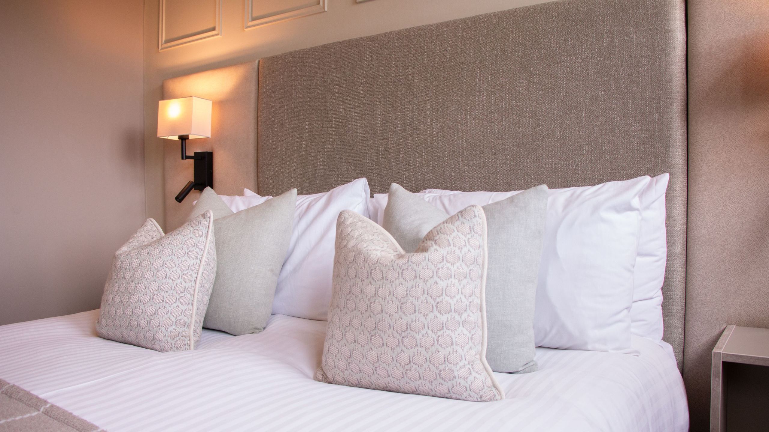 Neatly made bed with decorative pillows and a light-colored headboard in a modern bedroom