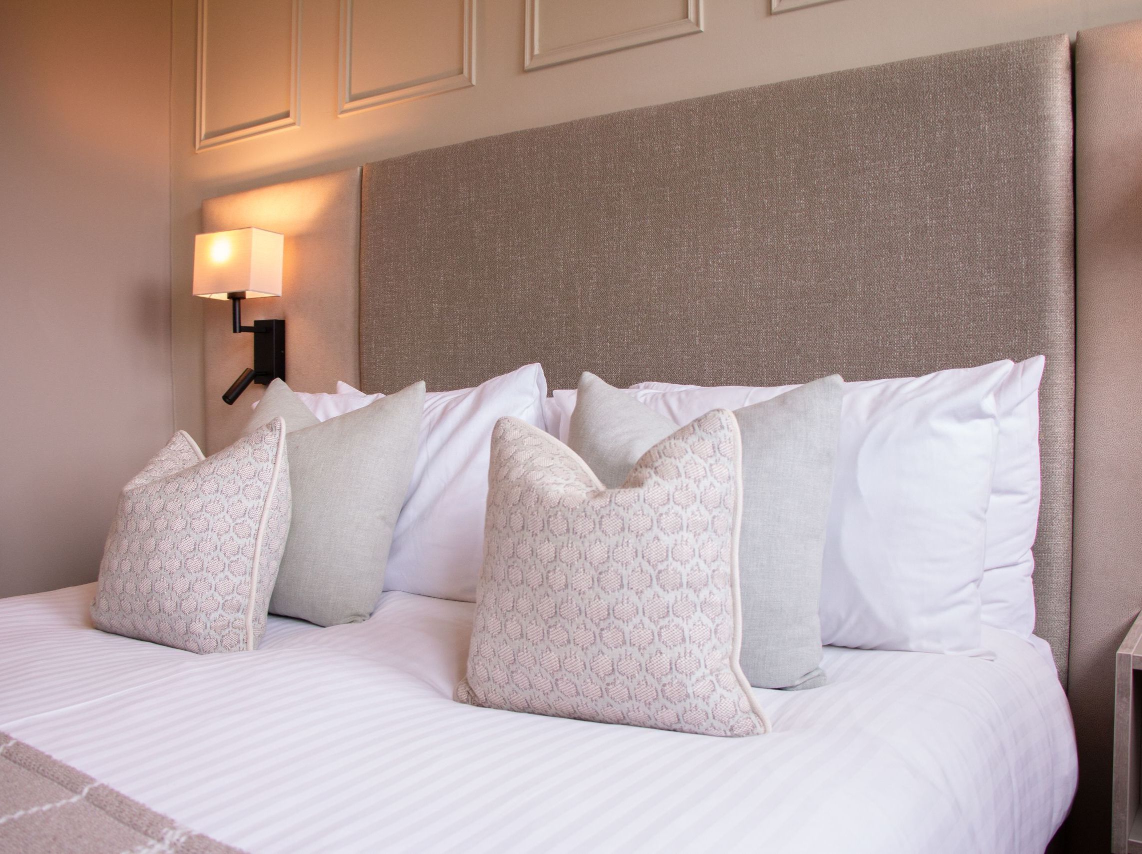 Neatly made bed with decorative pillows and a light-colored headboard in a modern bedroom