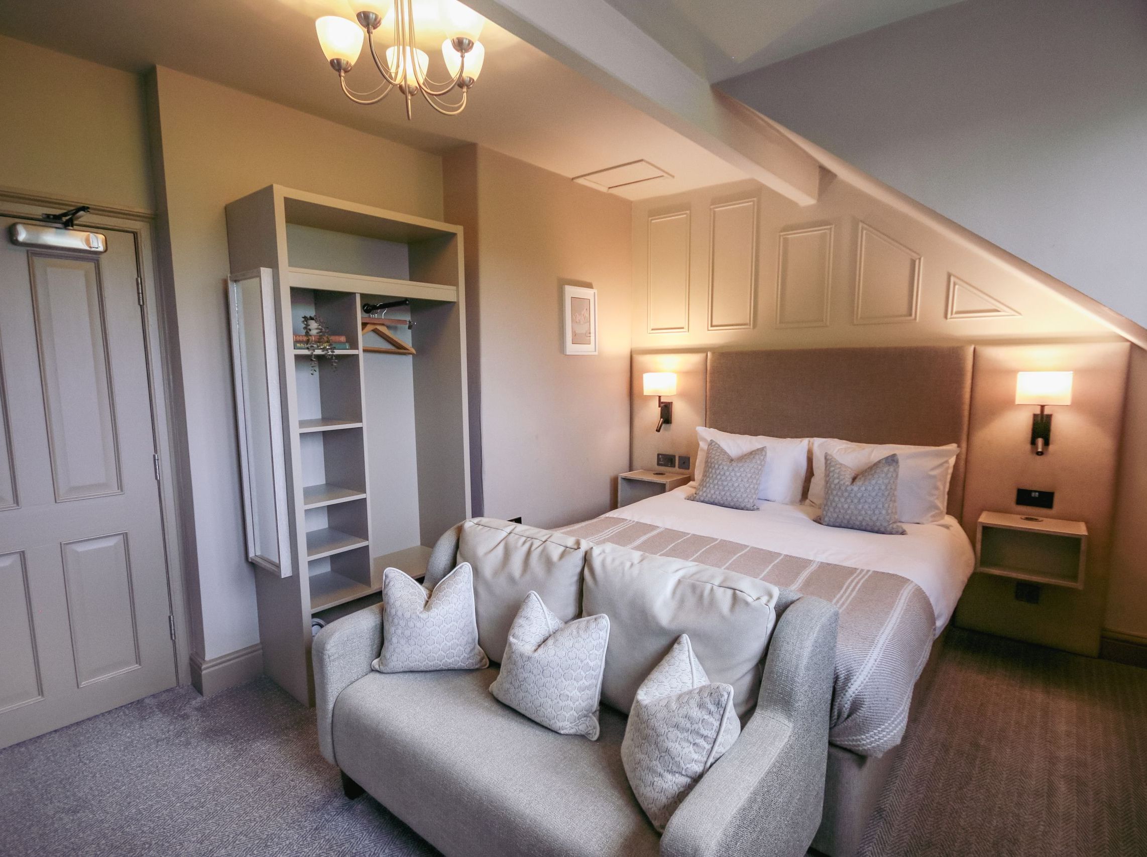 Cozy hotel room with a double bed, sofa, and open wardrobe under slanted ceiling