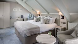 Modern hotel room with king-sized bed, armchair, and sloped ceiling