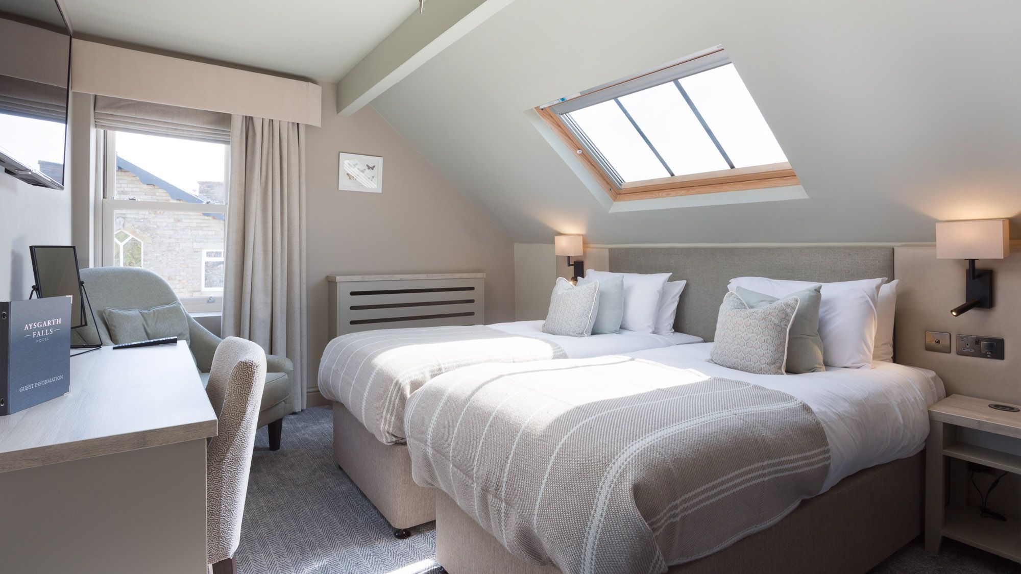Modern hotel room with two single beds, skylight, desk, and window.