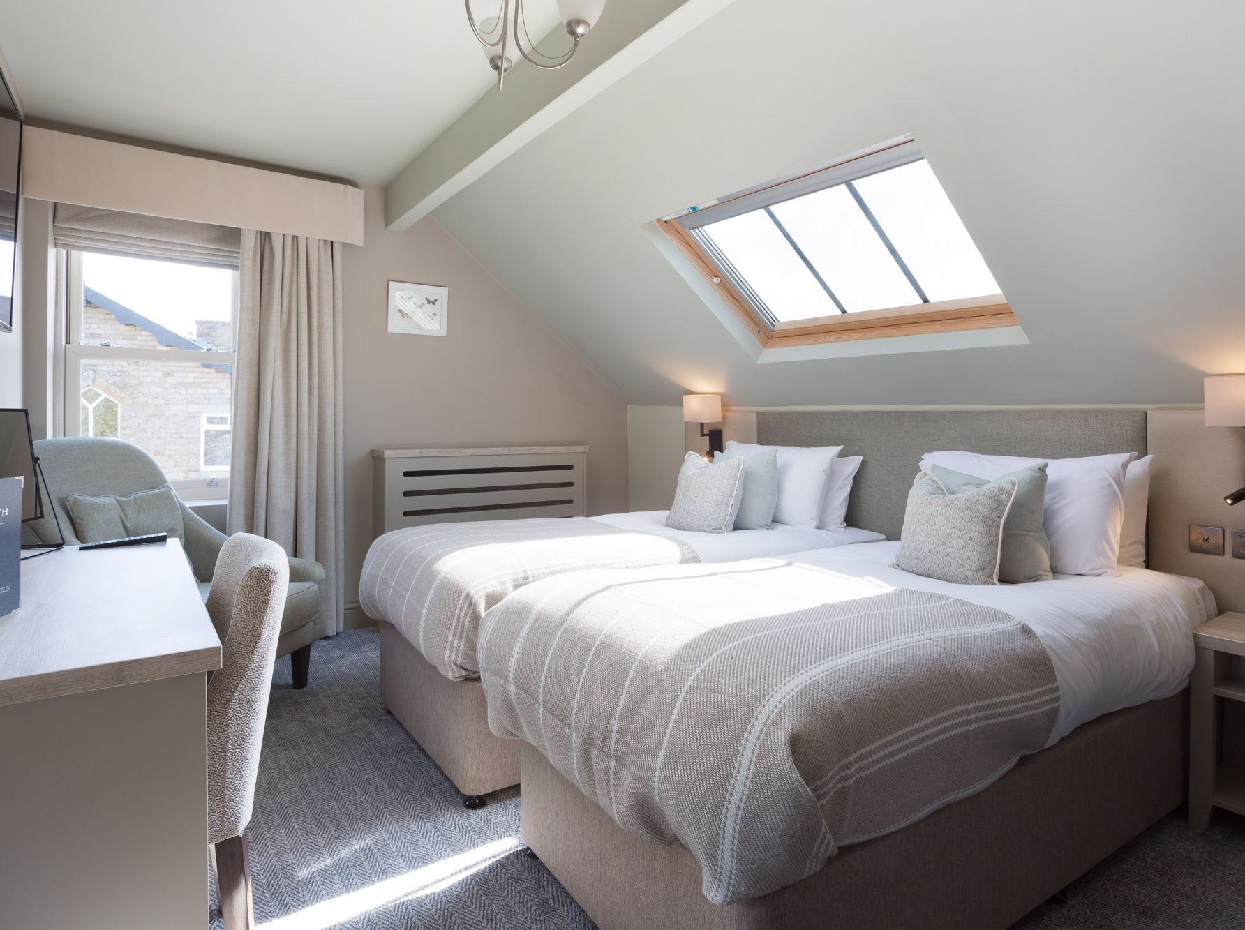 Modern hotel room with two single beds, skylight, desk, and window.
