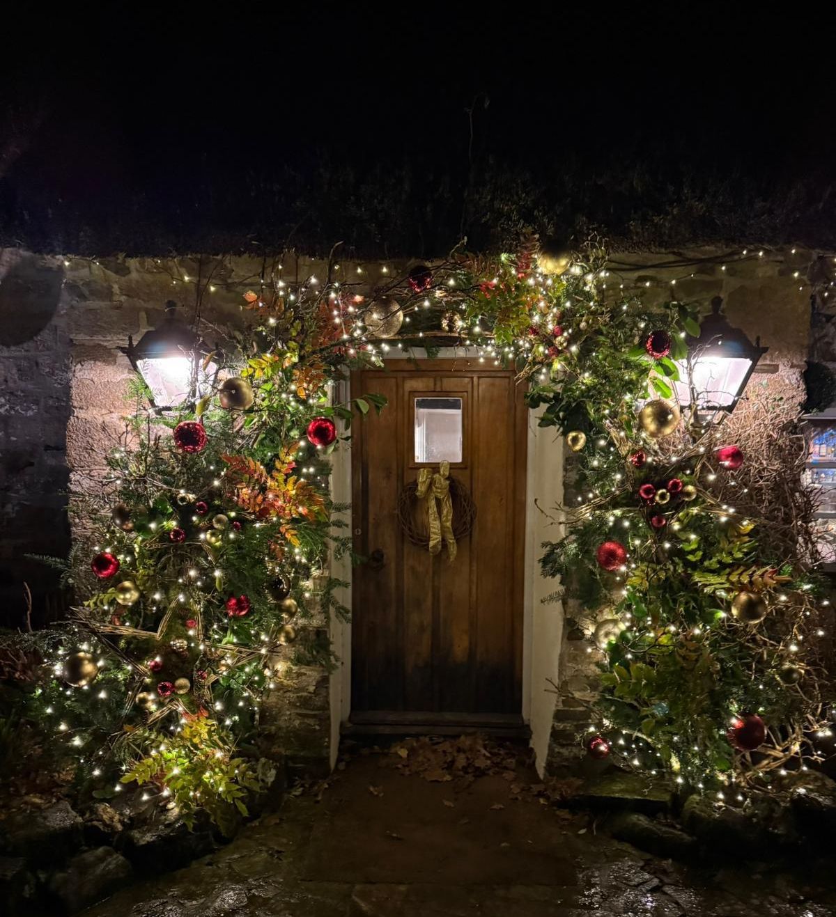 Rustic wooden door decorated with Christmas lights and ornaments at night