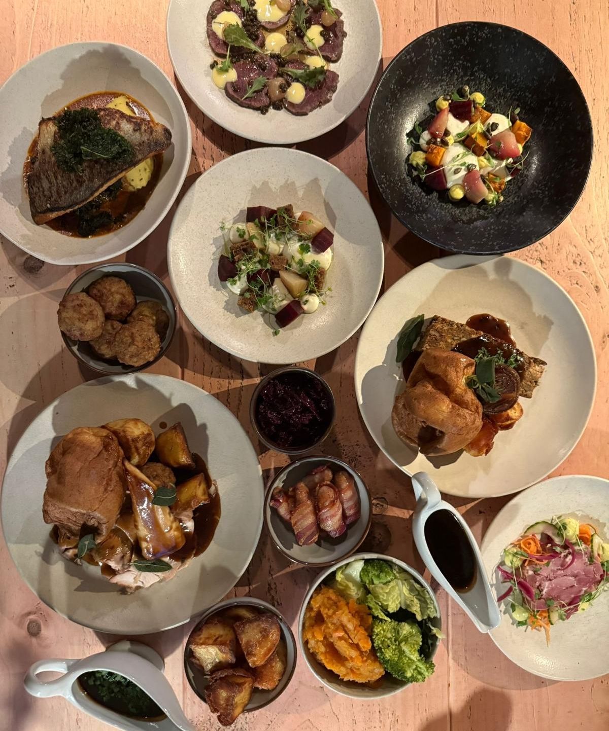 Assorted festive party dishes arranged on a wooden table, including roasted meats, vegetables, sides, and garnishes.