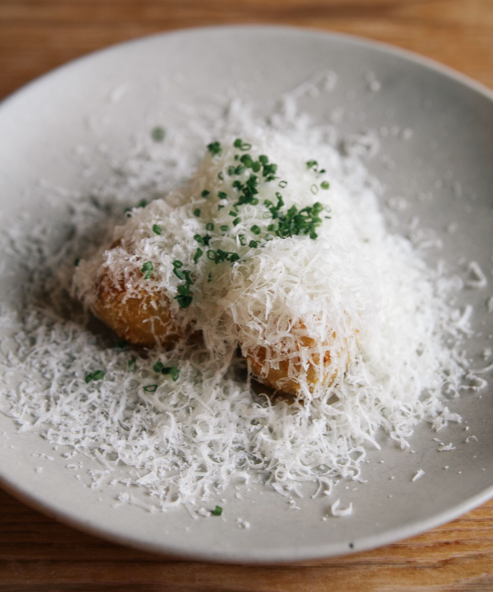 Potato croquettes topped with finely grated cheese and chopped chives on a white plate