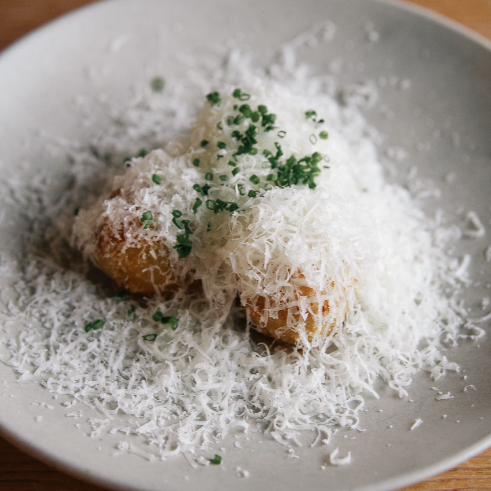 Potato croquettes topped with finely grated cheese and chopped chives on a white plate