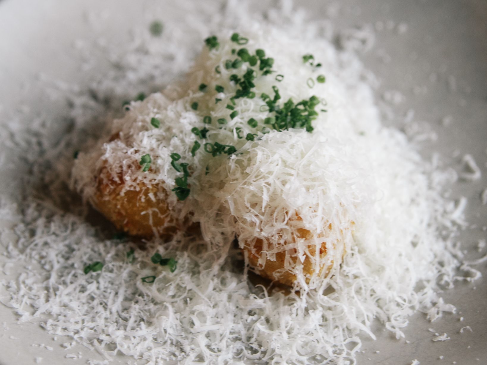 Potato croquettes topped with finely grated cheese and chopped chives on a white plate