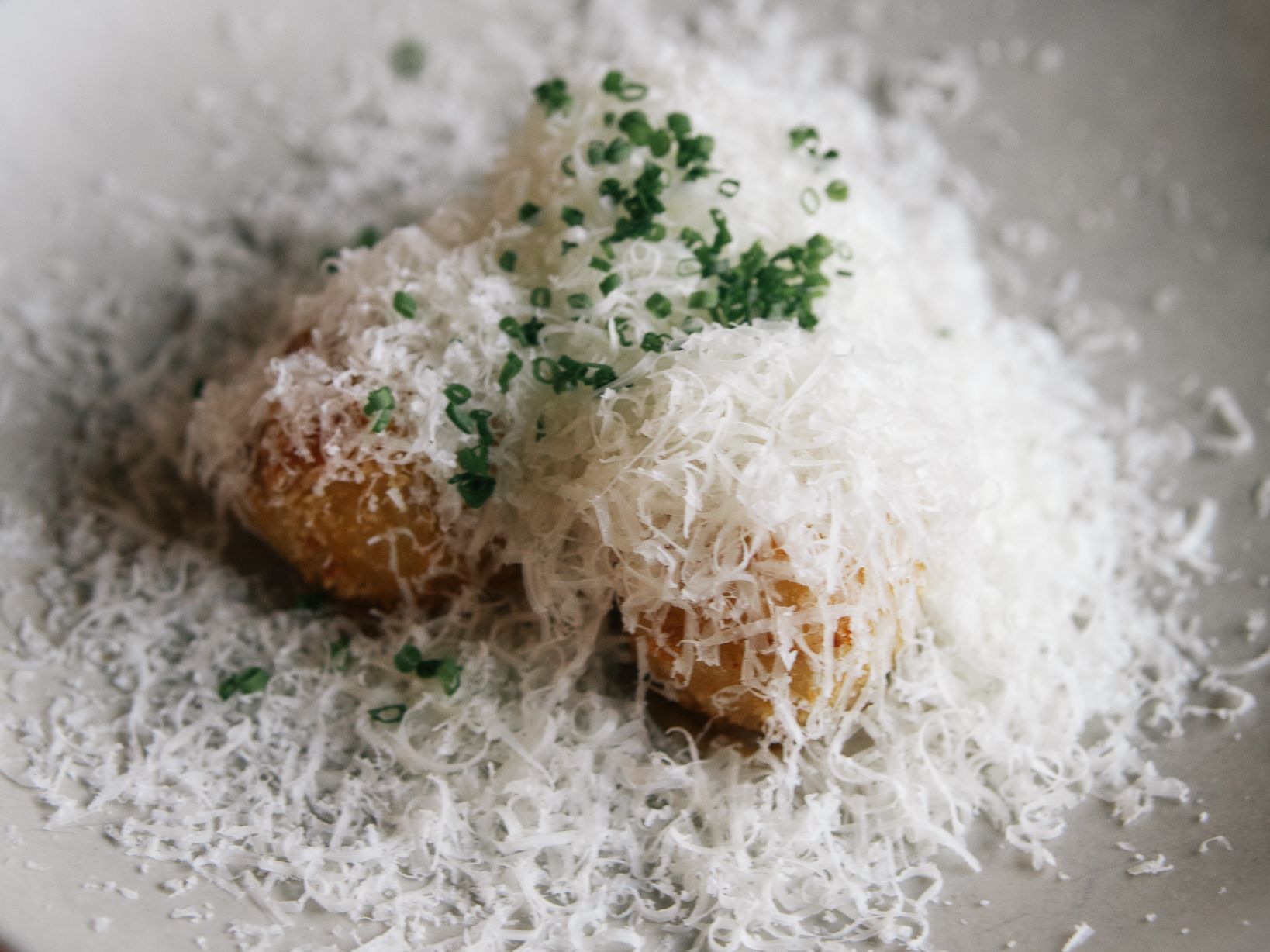 Potato croquettes topped with finely grated cheese and chopped chives on a white plate
