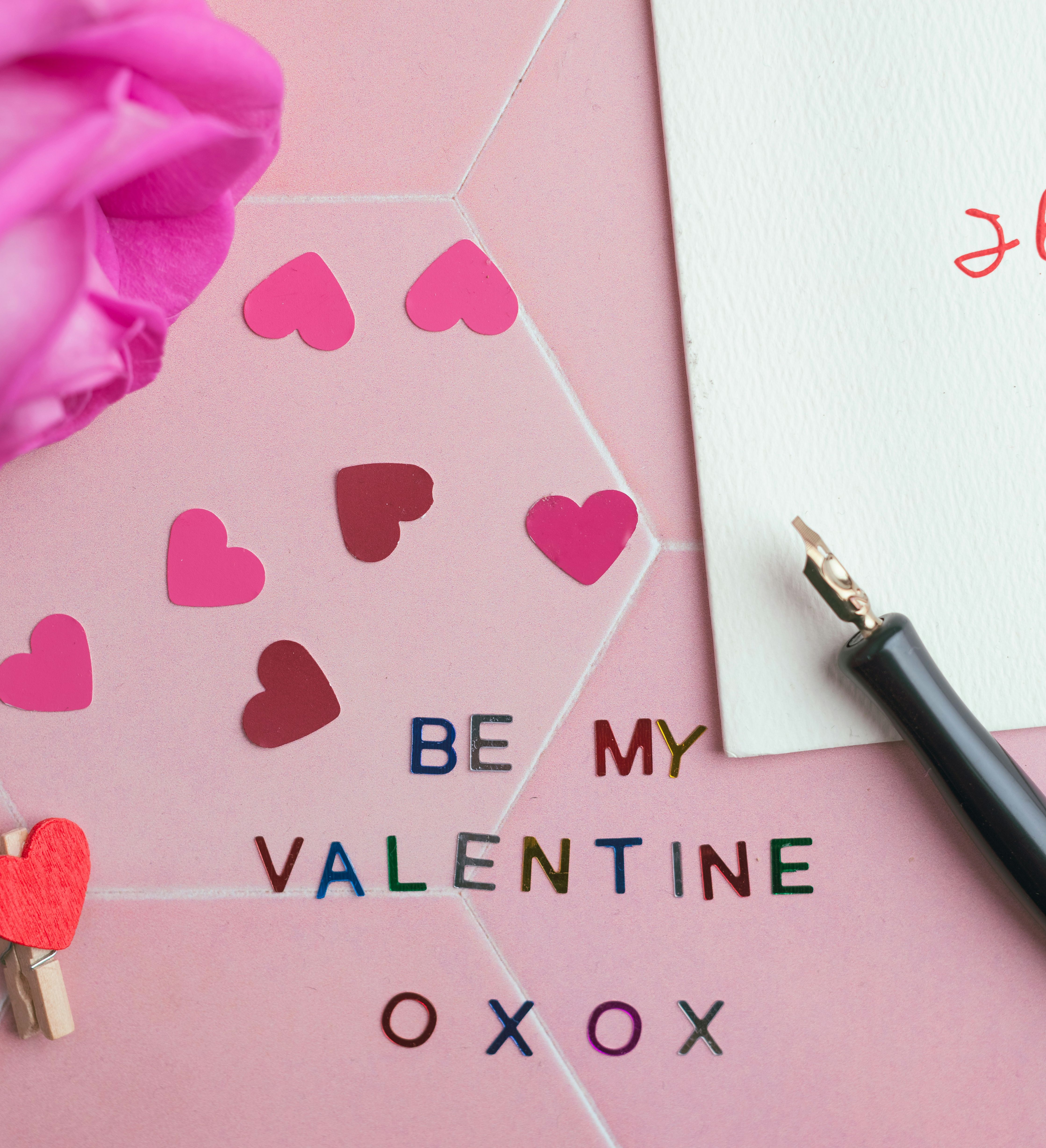Valentine's Day flat lay with pink rose, paper hearts, pen, and note reading 'I love you' on textured card