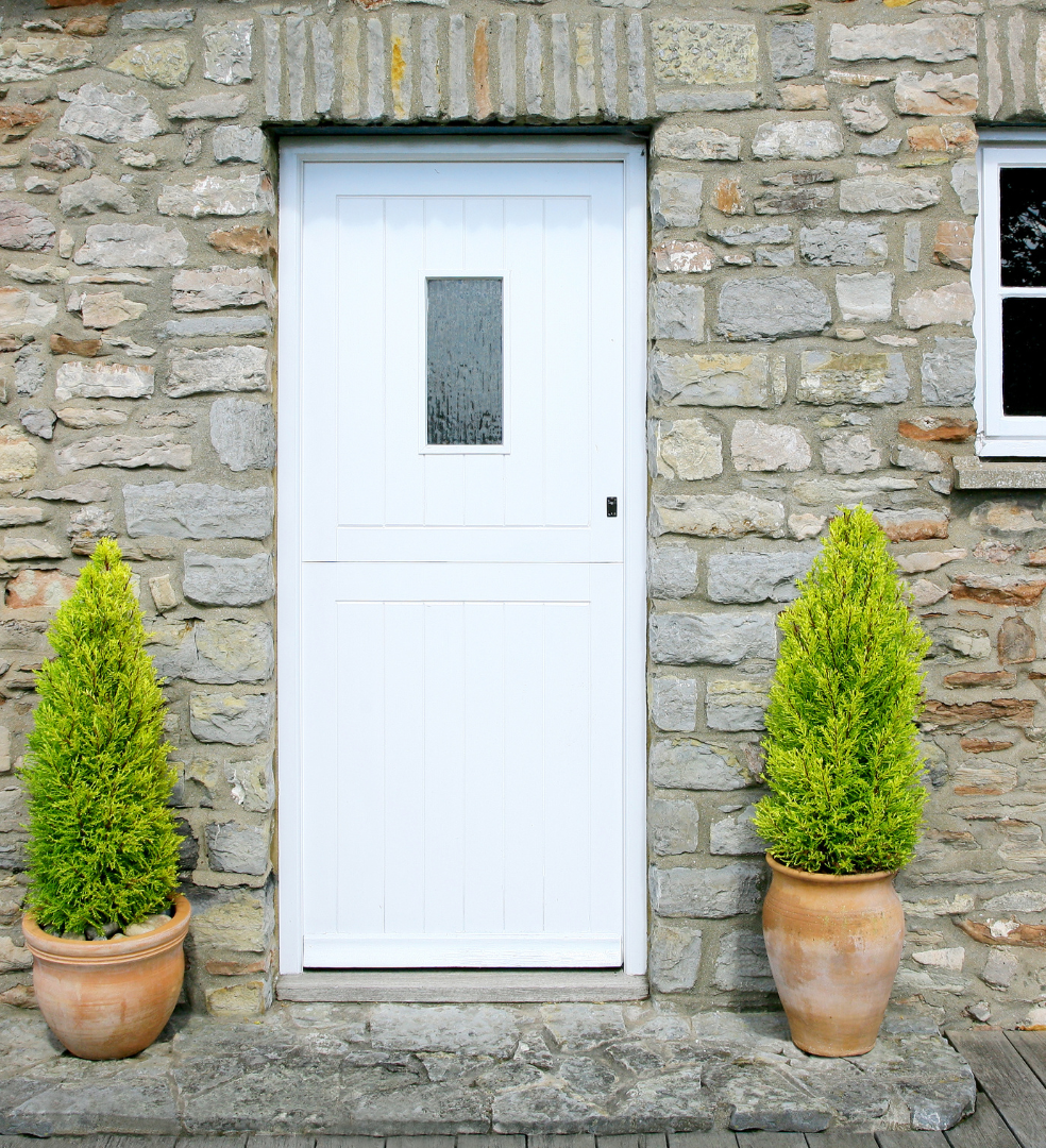 White door on a stone house with two potted shrubs on either side.