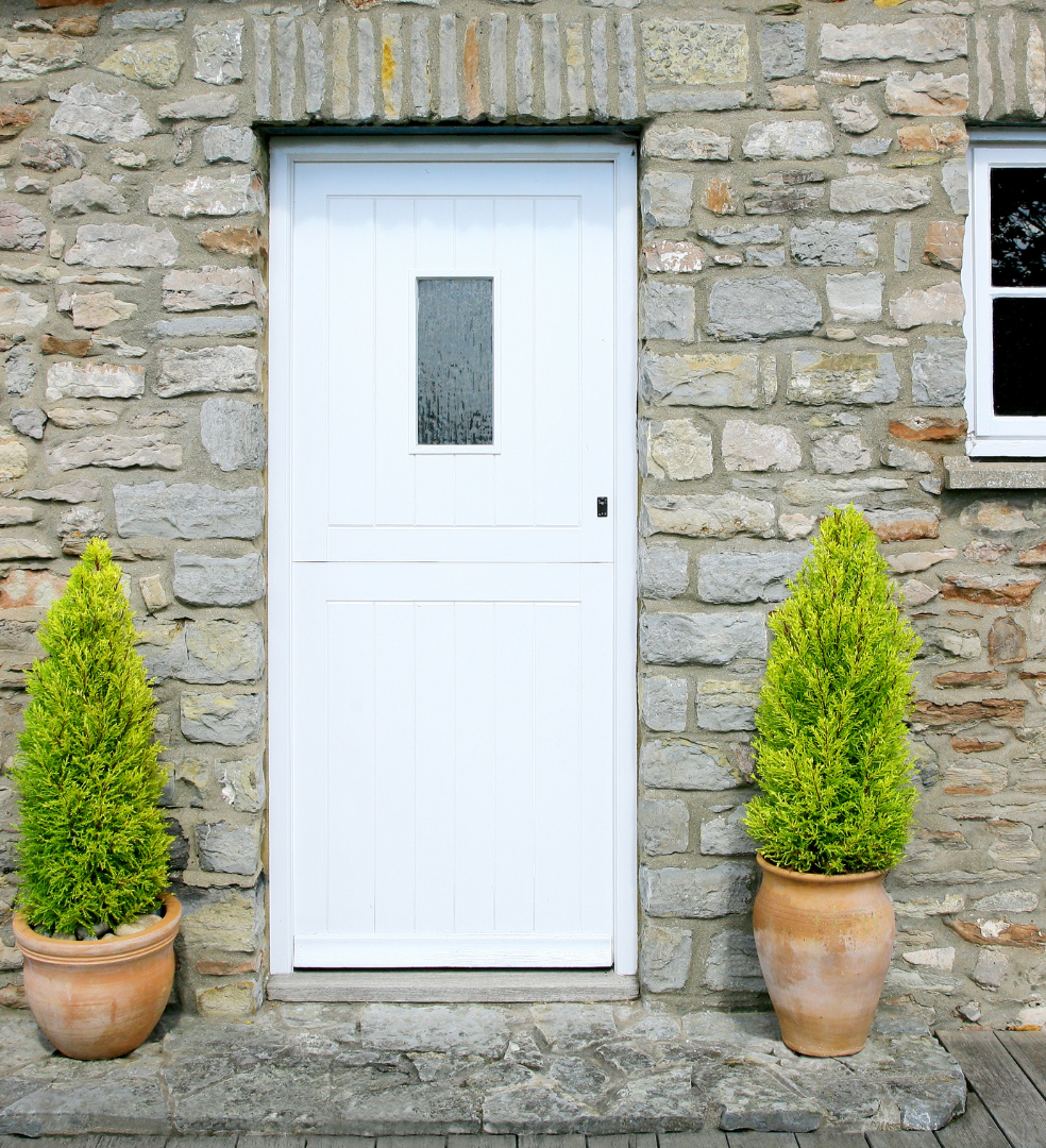 White door set in a stone wall with two potted evergreen plants on either side