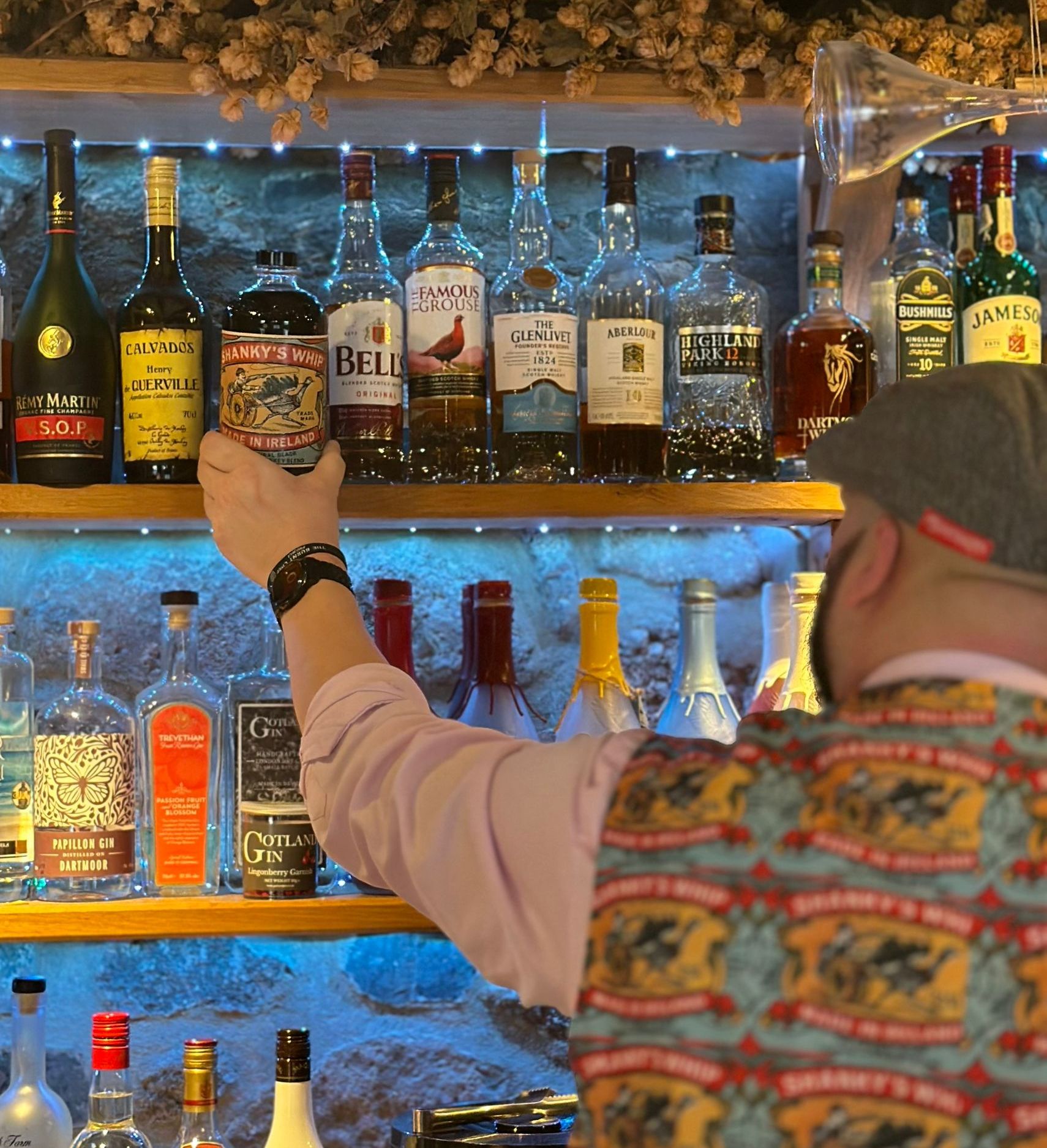 Bartender reaching for a bottle of Shanky's Whip on a well-stocked bar shelf