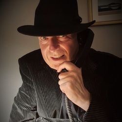 Man in a pinstripe suit and black hat speaking on a corded telephone.