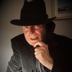 Man in a pinstripe suit and black hat speaking on a corded telephone.