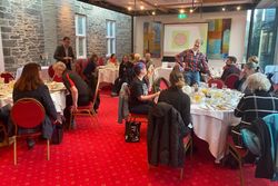 Group of people sitting at round tables having breakfast in a conference room with a projector screen displaying 'Tavistock Plan'.