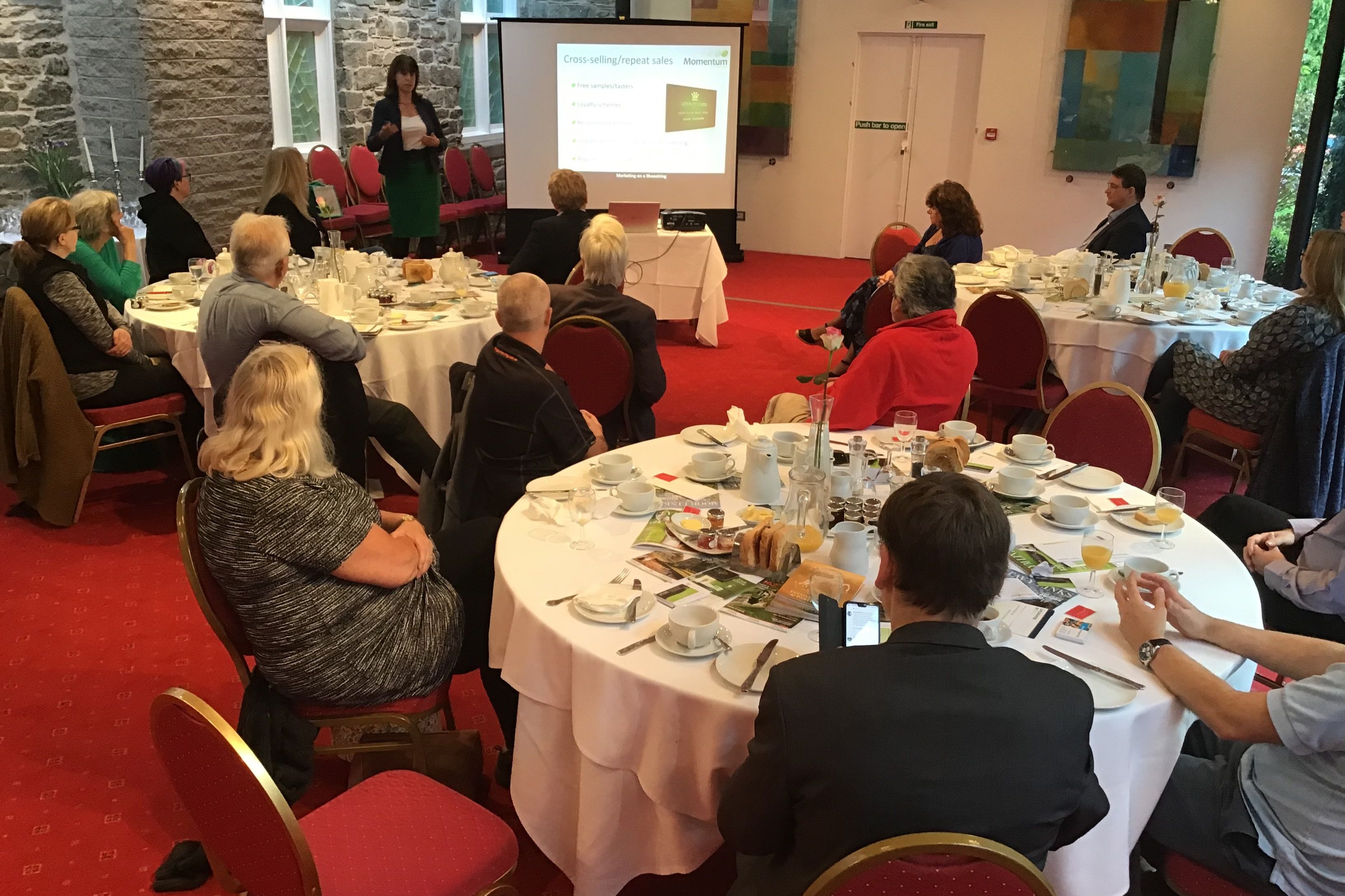 People attending a breakfast meeting with a presenter speaking in front of a screen.