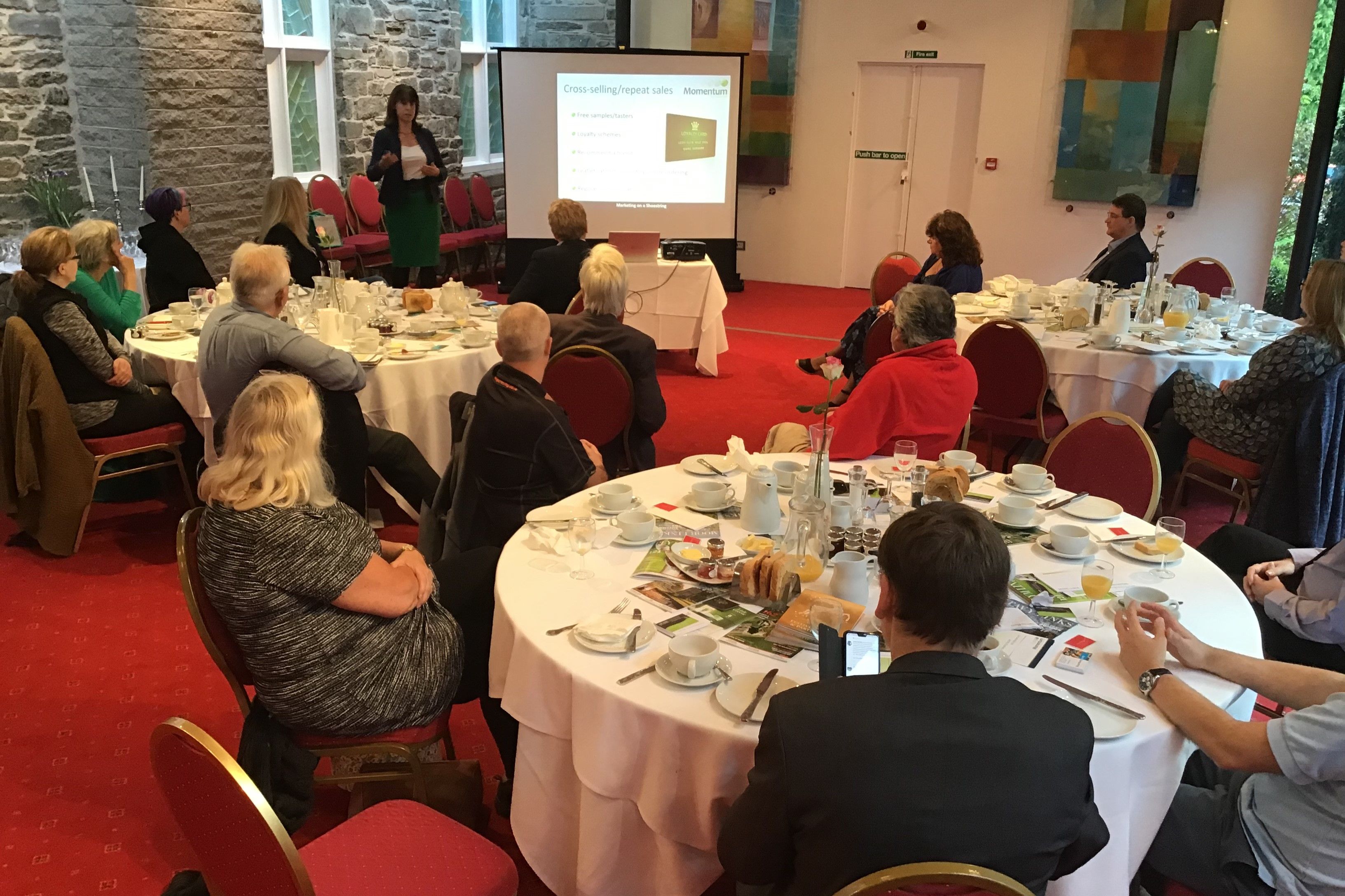 People attending a breakfast meeting with a presenter speaking in front of a screen.
