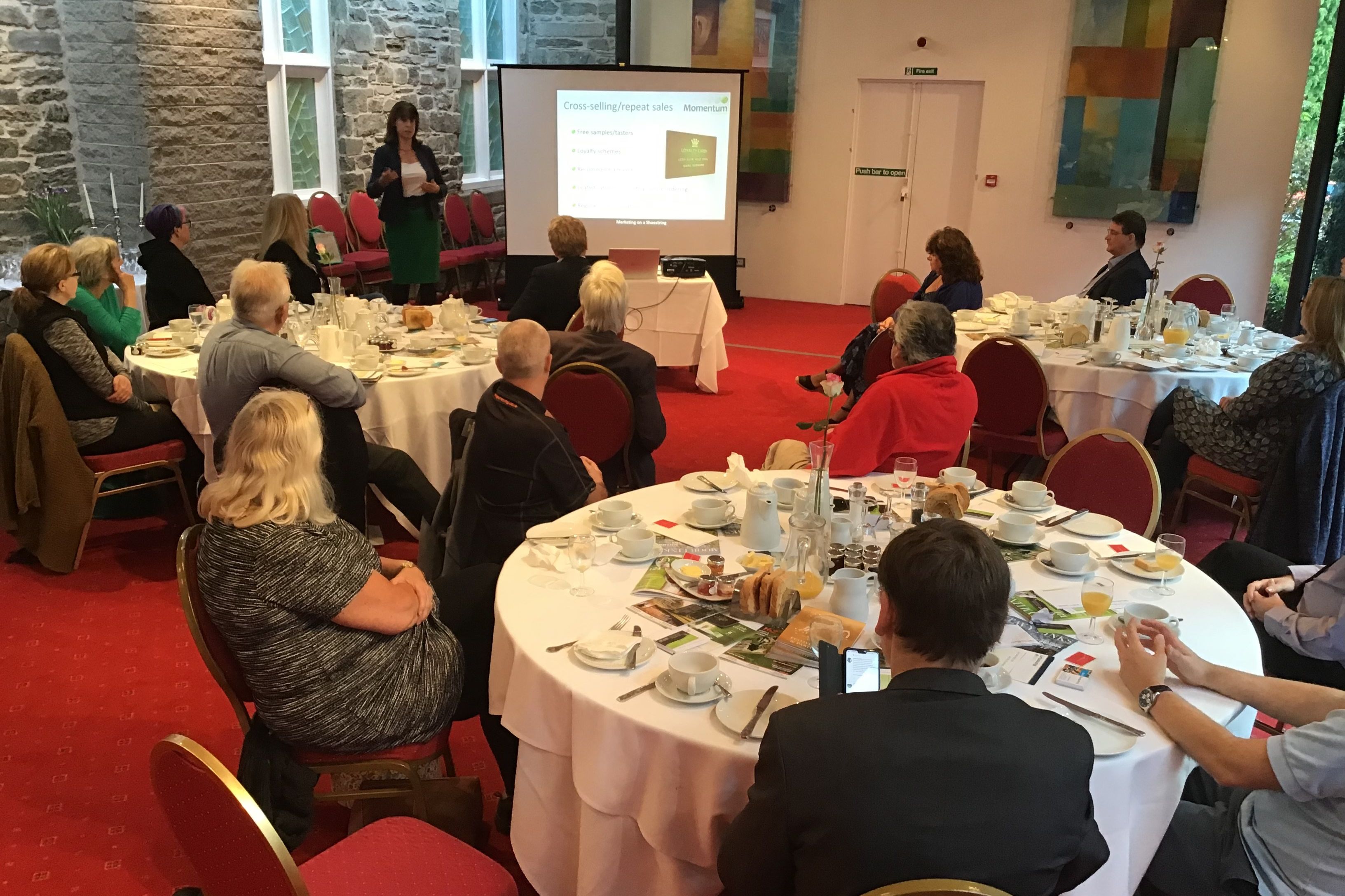 People attending a breakfast meeting with a presenter speaking in front of a screen.