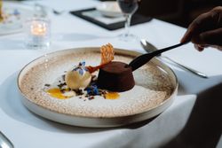 A decadent gourmet dessert with chocolate cake, a scoop of vanilla ice cream, and decorative edible flowers on a patterned plate.