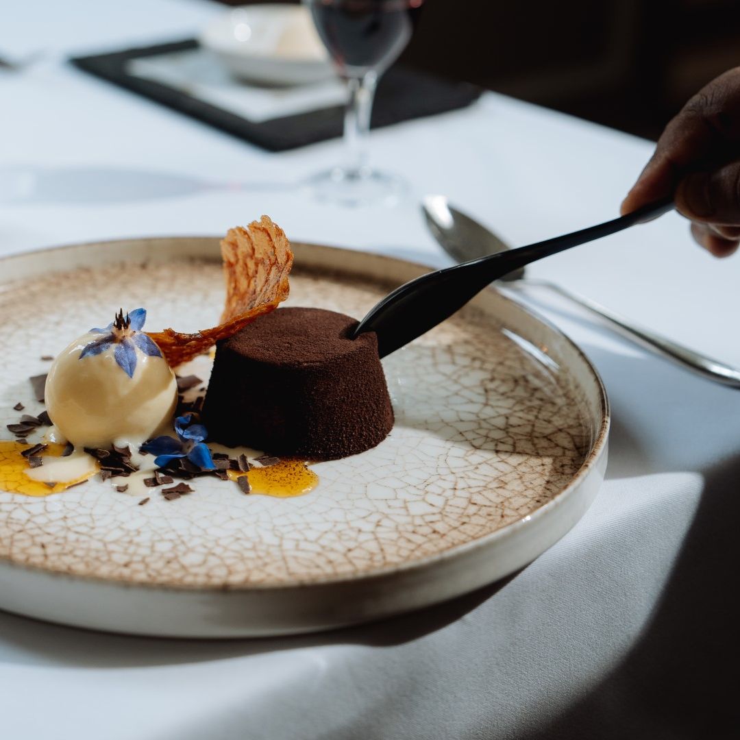 A decadent gourmet dessert with chocolate cake, a scoop of vanilla ice cream, and decorative edible flowers on a patterned plate.