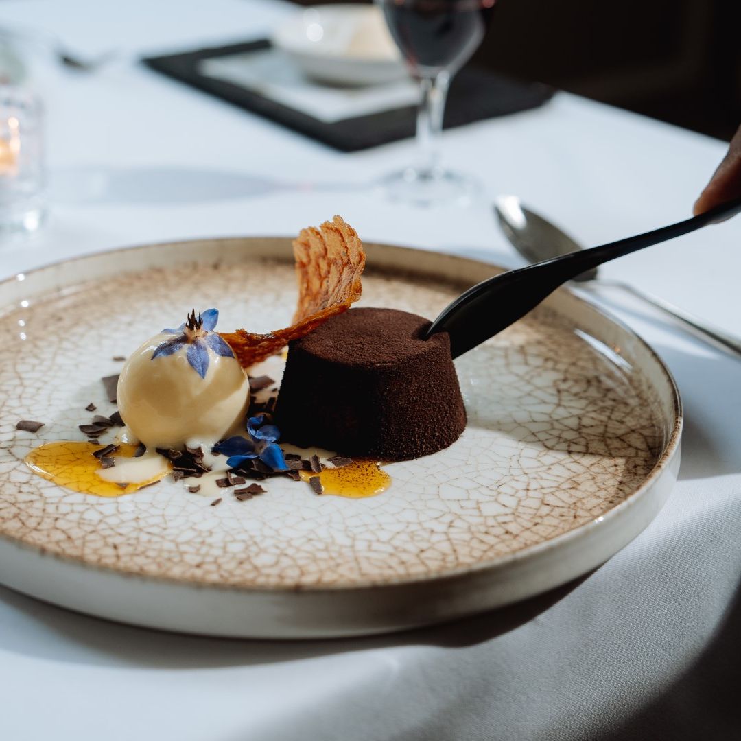 A decadent gourmet dessert with chocolate cake, a scoop of vanilla ice cream, and decorative edible flowers on a patterned plate.