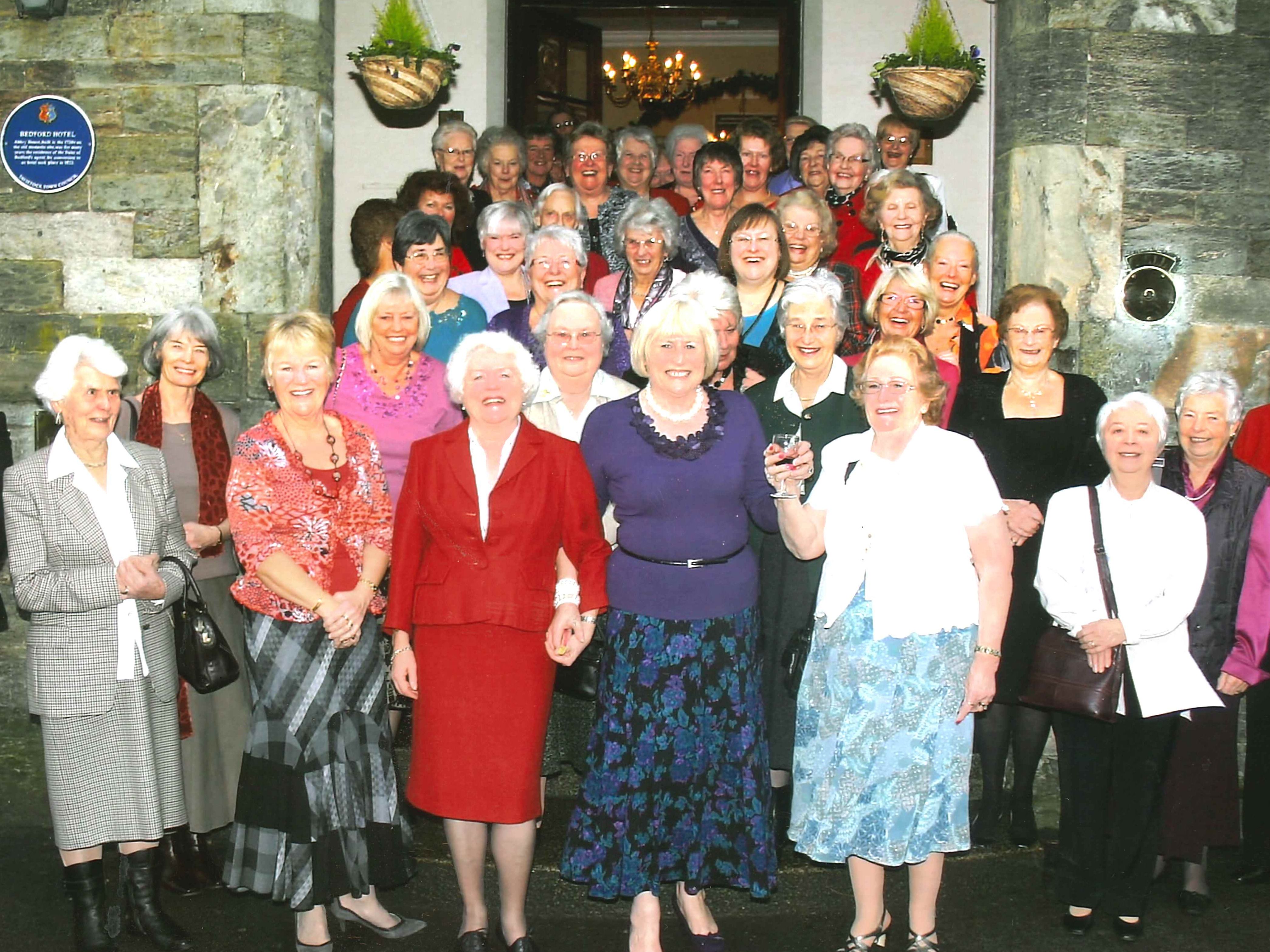 A large group of older women standing together outside the Bedford Hotel, posing for a group photo.