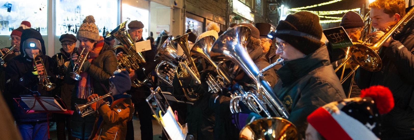 Brass band playing music outdoors during a festive night event, with people wearing warm winter clothing and hats.