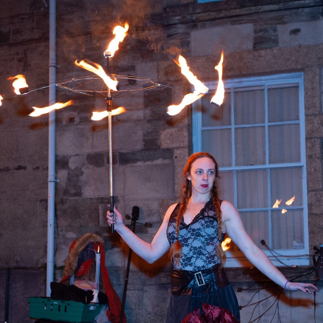 Performer with braided hair holding a fire spinning staff in front of a stone building at night