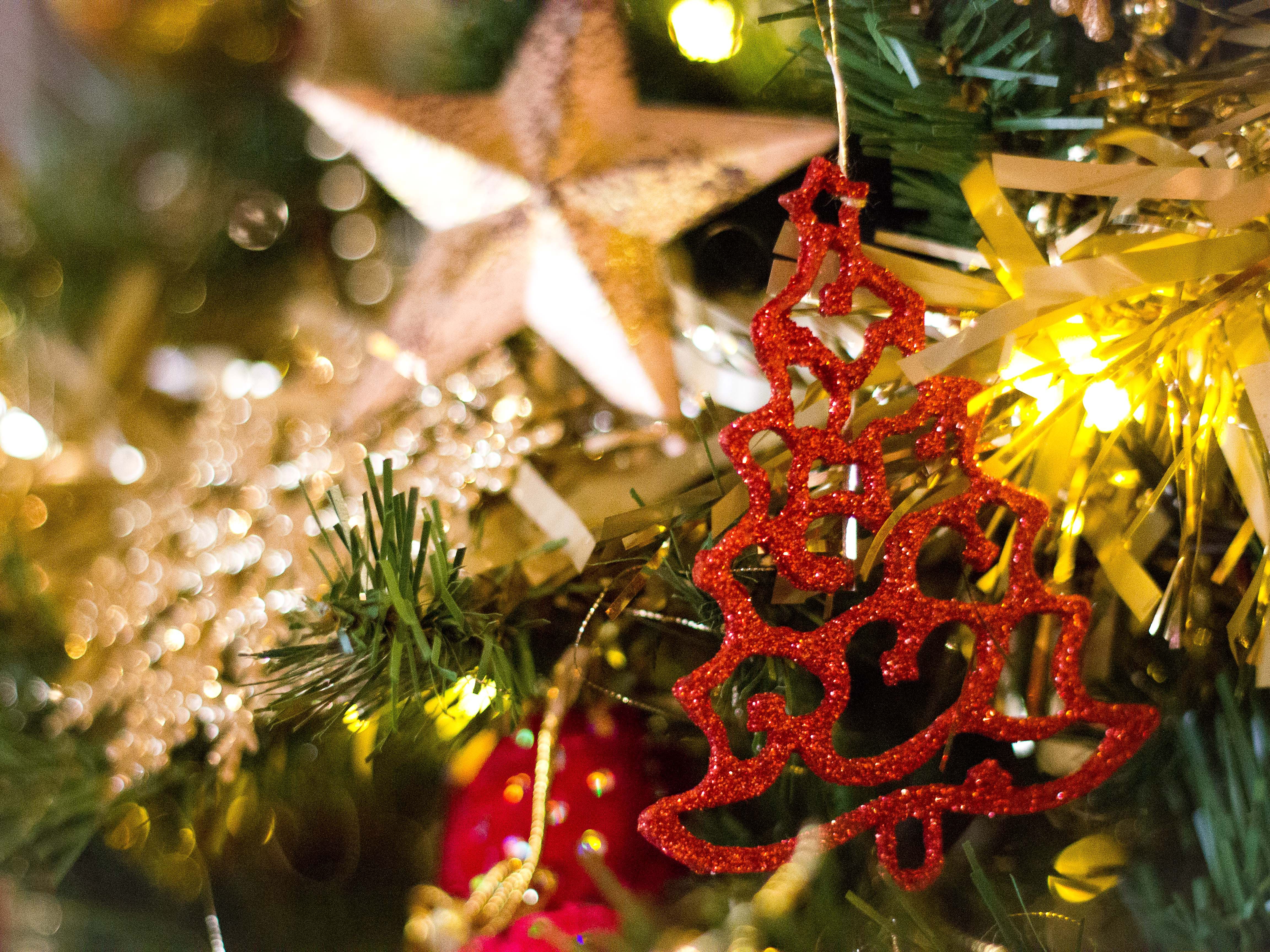 Close-up of a Christmas tree decorated with a sparkling red tree ornament, golden tinsel, and a large star ornament.