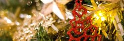 Close-up of a Christmas tree decorated with a sparkling red tree ornament, golden tinsel, and a large star ornament.