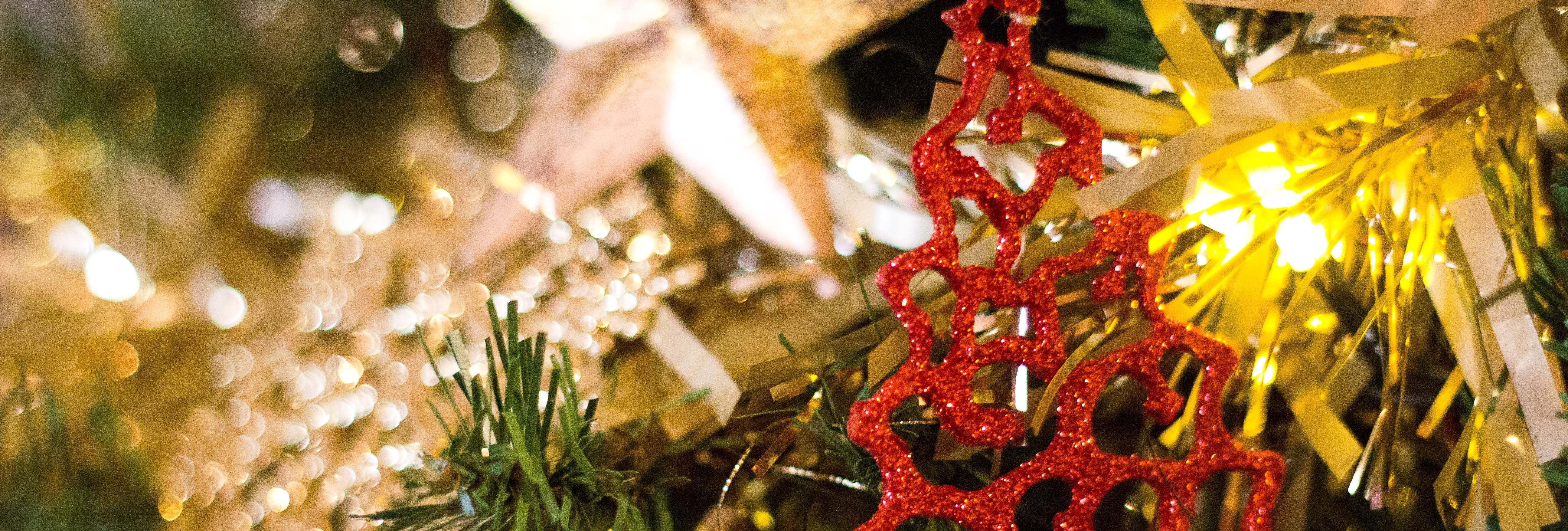 Close-up of a Christmas tree decorated with a sparkling red tree ornament, golden tinsel, and a large star ornament.