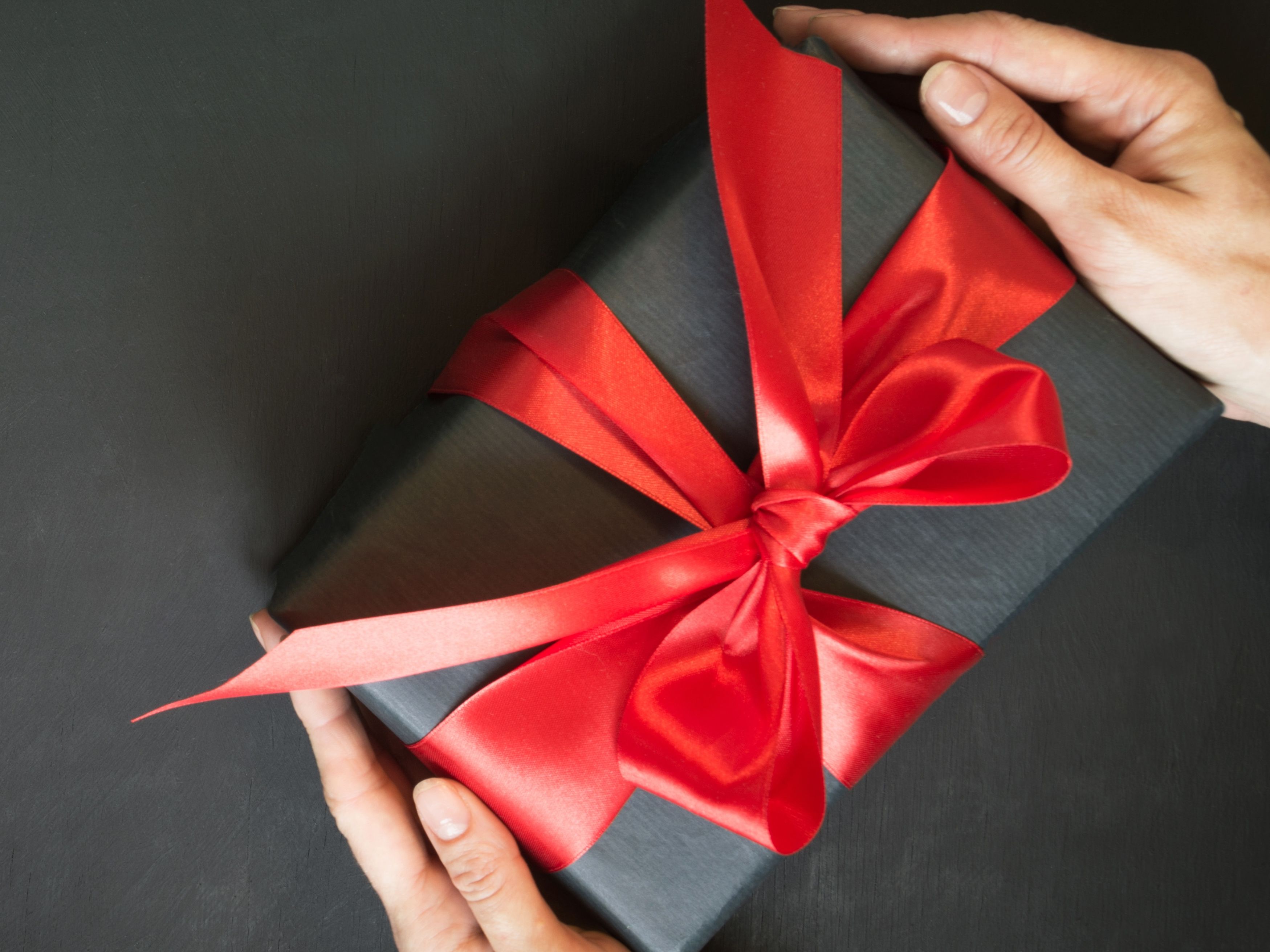 Person holding a gift box with a red ribbon on a black background