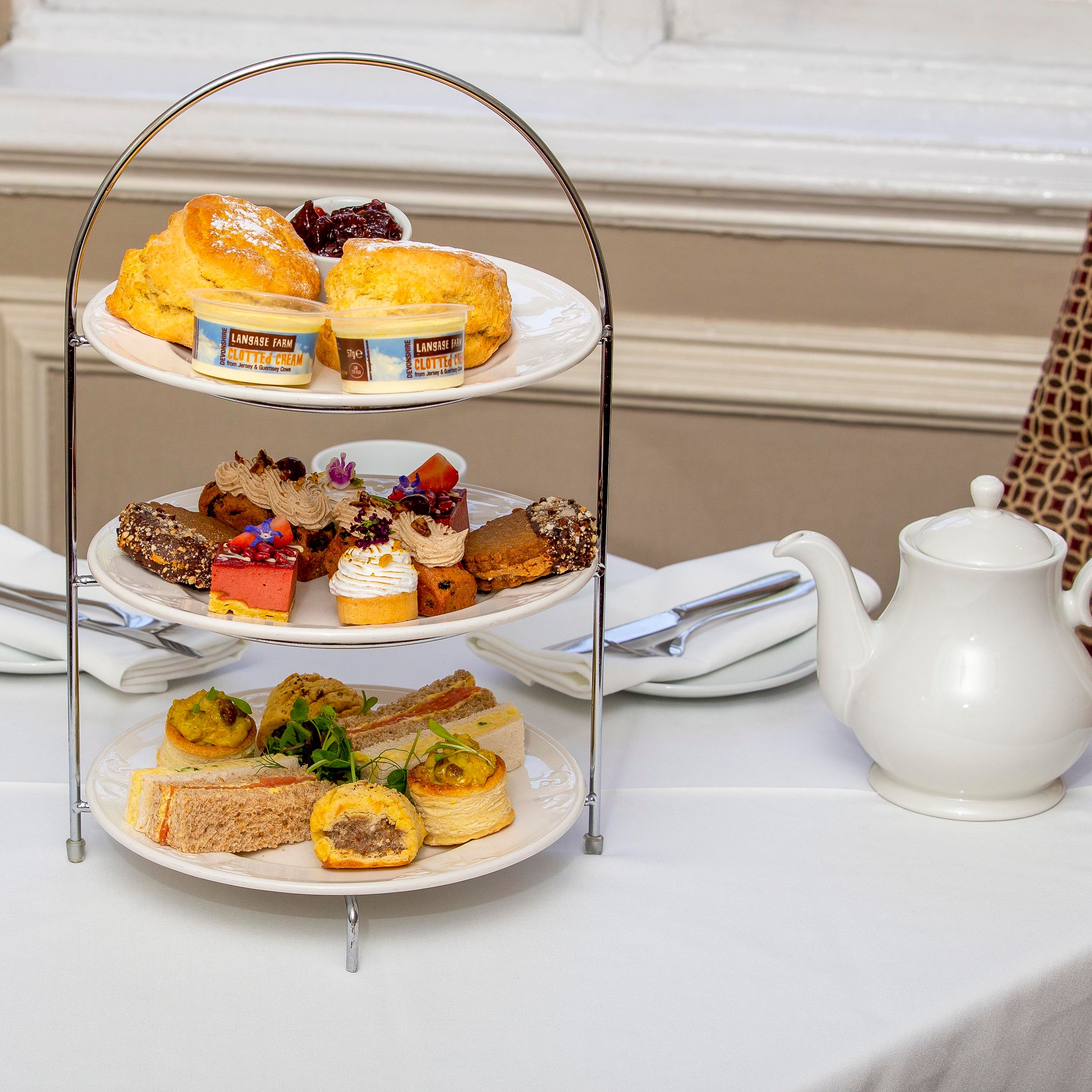 Three-tiered tray with scones, desserts, and sandwiches for afternoon tea.