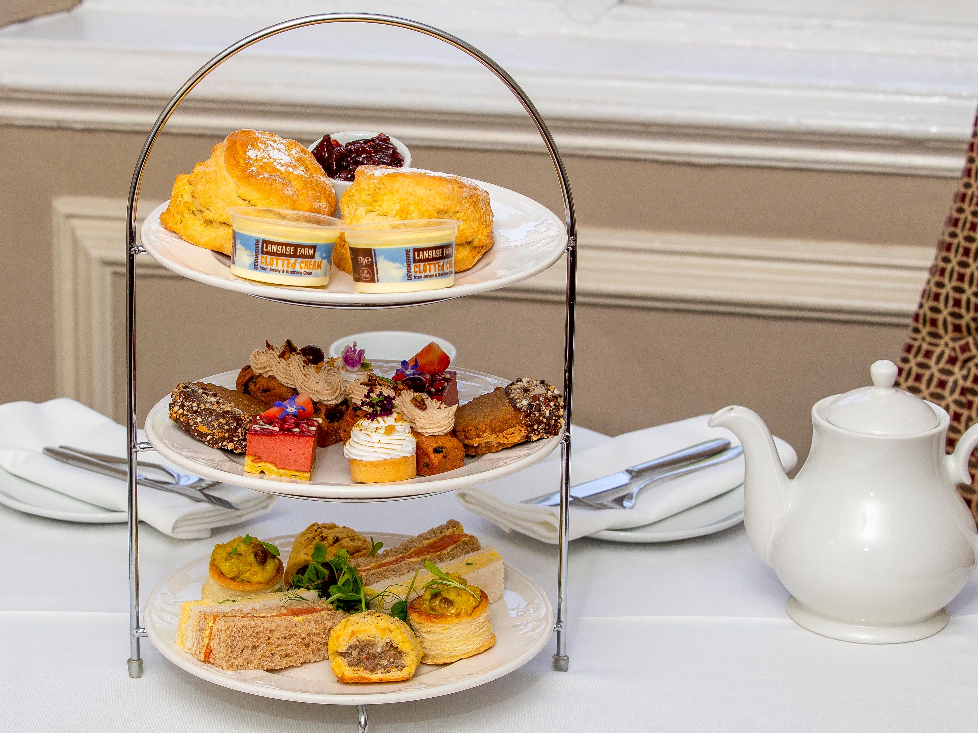 Three-tiered tray with scones, desserts, and sandwiches for afternoon tea.