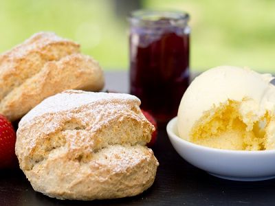 A plate with scones, clotted cream, a jar of strawberry jam, and fresh strawberries.