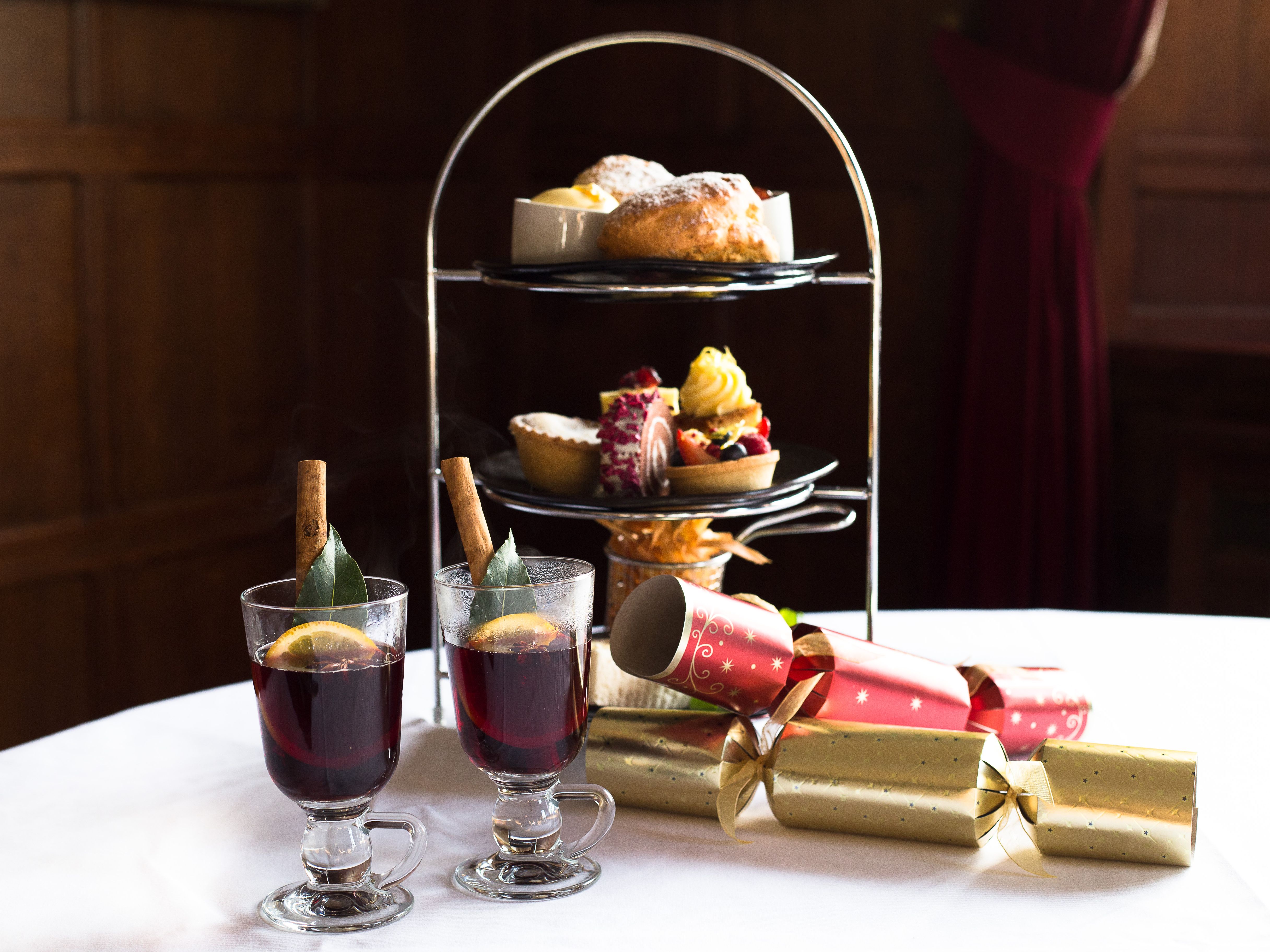 Festive afternoon tea set with pastries, desserts, mulled wine, and Christmas crackers on a white tablecloth