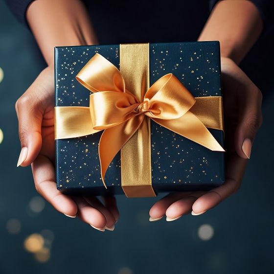 Hands holding a blue gift box with a gold ribbon bow