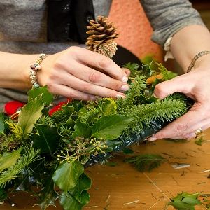 Person decorating a wreath with greenery and a pine cone
