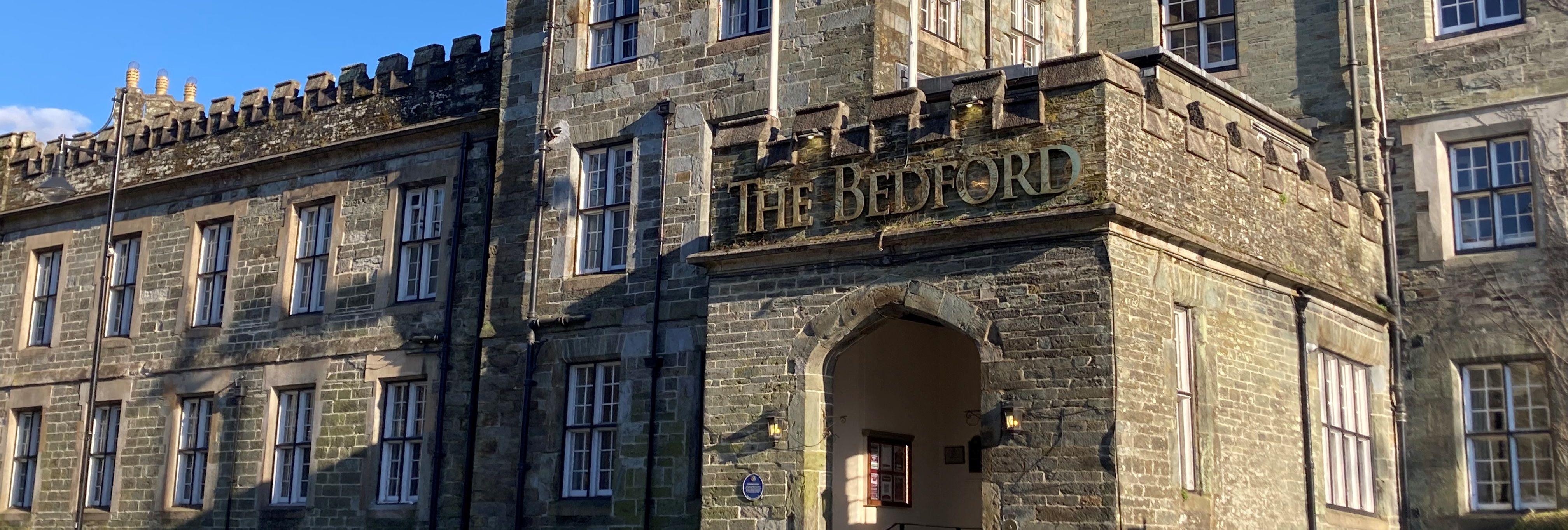Historic stone building named The Bedford with flags flying above the entrance on a sunny day