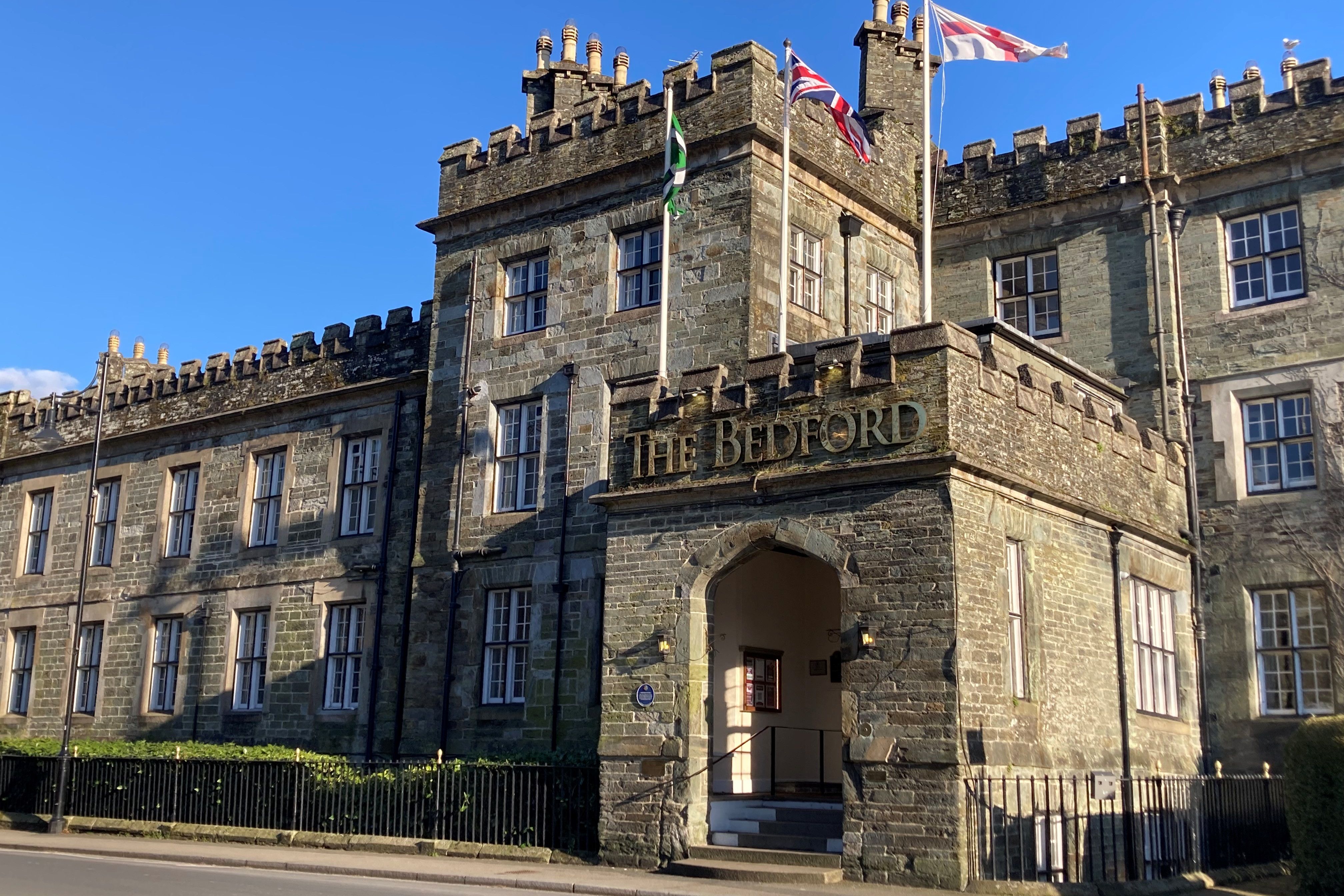 Historic stone building named The Bedford with flags flying above the entrance on a sunny day