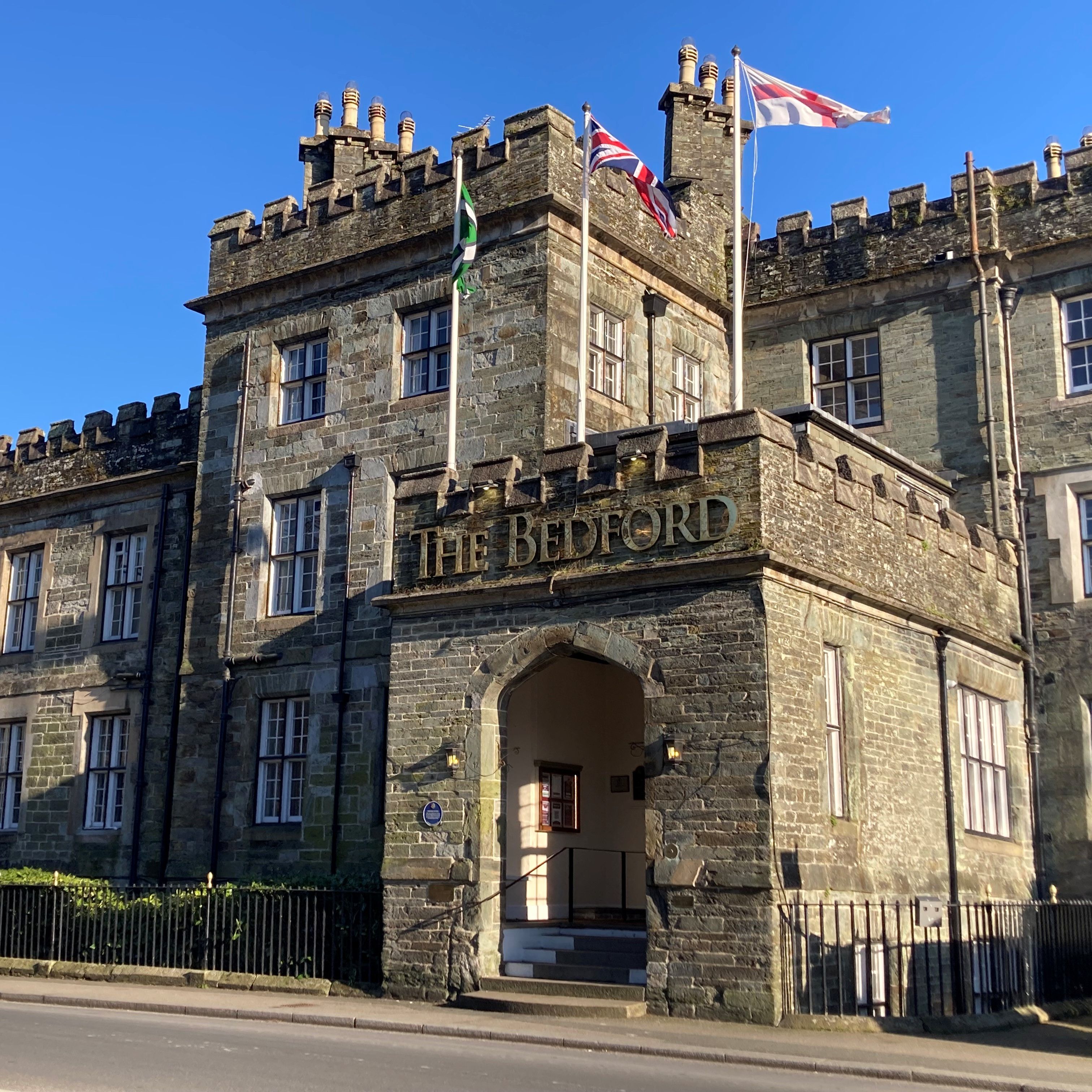 Historic stone building named The Bedford with flags flying above the entrance on a sunny day