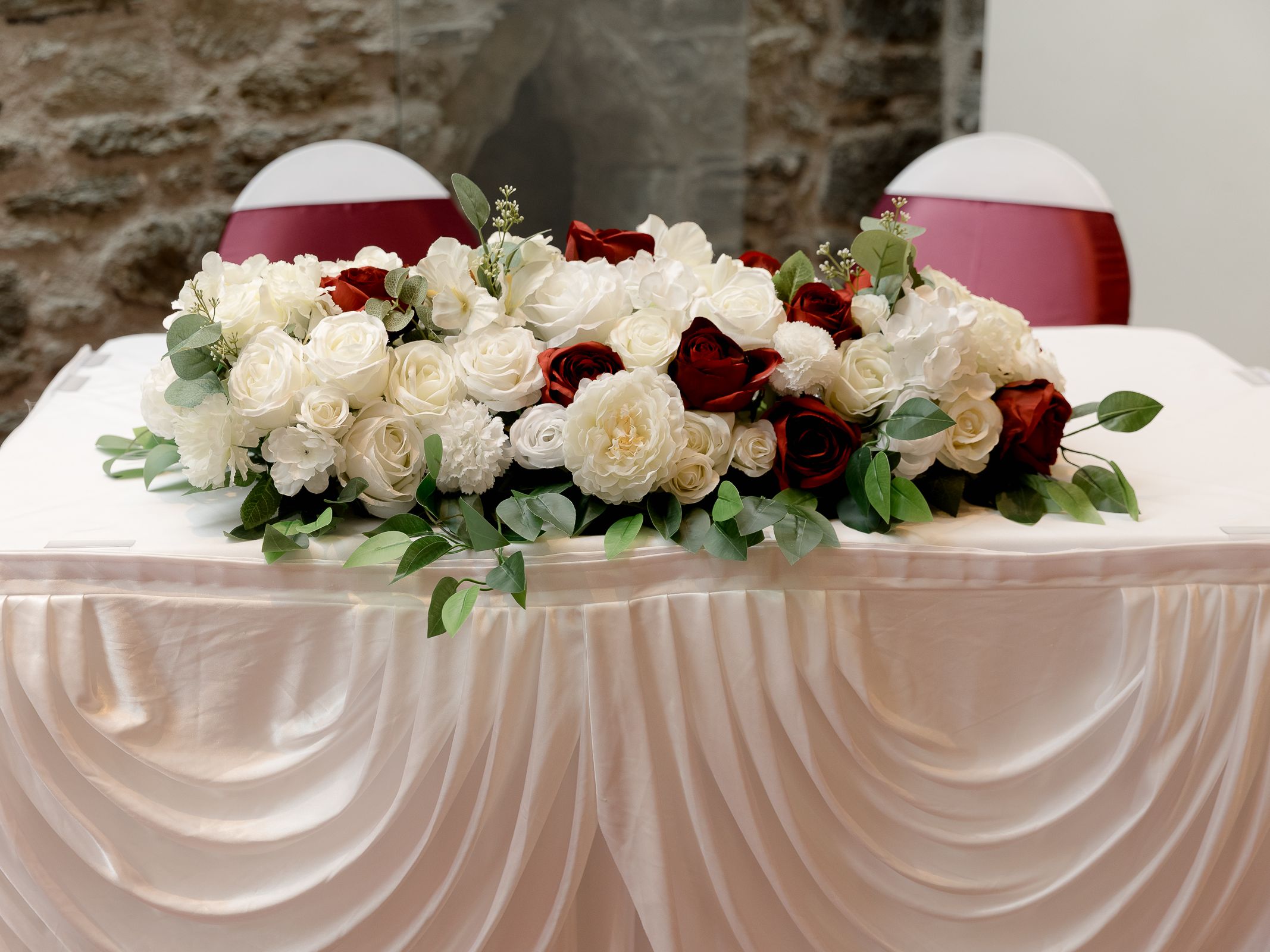 White table with a floral arrangement of white and red roses and green leaves