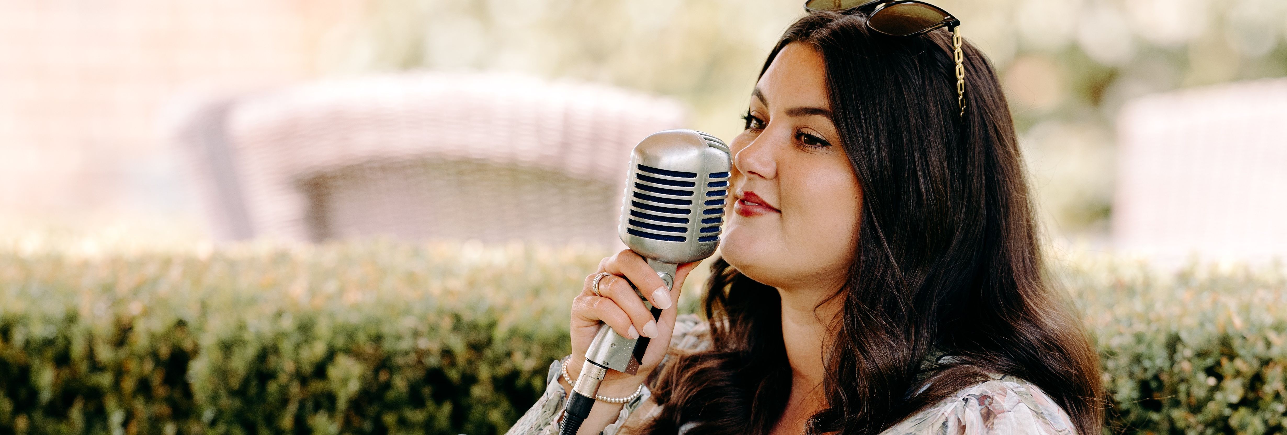 Woman in a floral dress singing into a vintage microphone outdoors